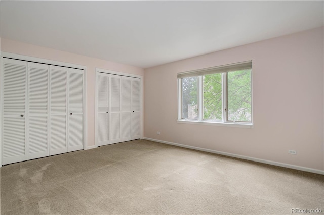 unfurnished bedroom featuring carpet flooring, two closets, and baseboards