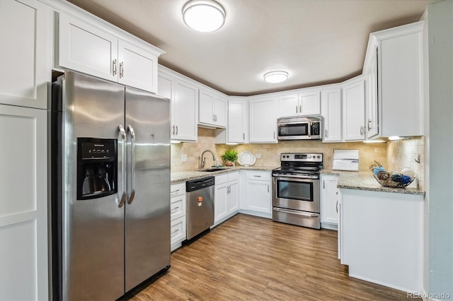 kitchen featuring appliances with stainless steel finishes, tasteful backsplash, white cabinetry, sink, and light stone counters