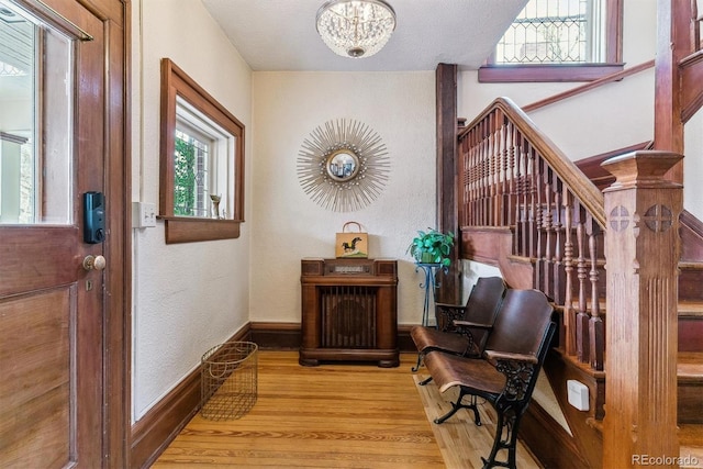 foyer entrance featuring stairs, a textured wall, wood finished floors, baseboards, and a notable chandelier