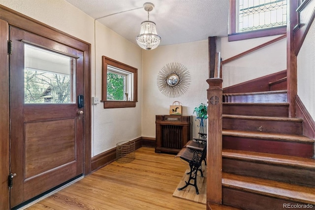 entryway featuring an inviting chandelier, a textured wall, stairway, a textured ceiling, and light wood finished floors