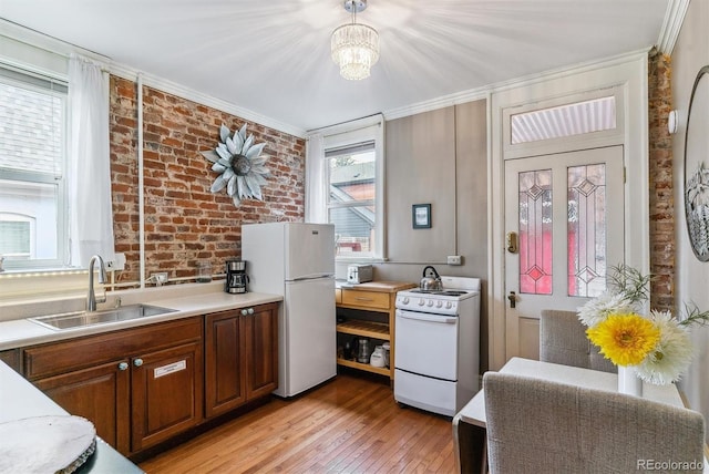 kitchen with brick wall, white appliances, light wood-type flooring, light countertops, and a sink