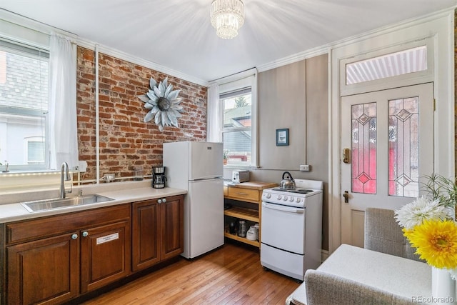 kitchen featuring brick wall, light wood-type flooring, a sink, light countertops, and white appliances