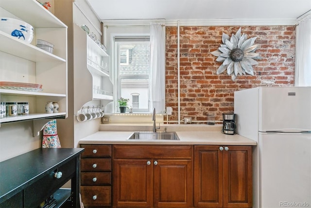 kitchen with open shelves, freestanding refrigerator, brick wall, light countertops, and a sink