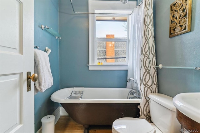 bathroom with toilet, a freestanding bath, a sink, and wood finished floors