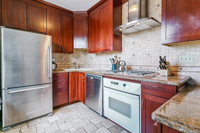 kitchen featuring wall chimney range hood, decorative backsplash, appliances with stainless steel finishes, dark brown cabinets, and a sink