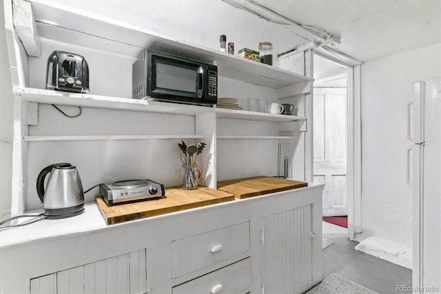 room details featuring black microwave, freestanding refrigerator, and finished concrete floors