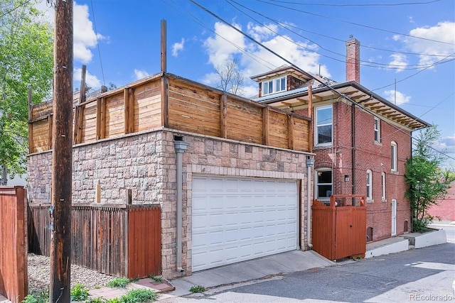 view of side of property with a garage, fence, a chimney, and stone siding