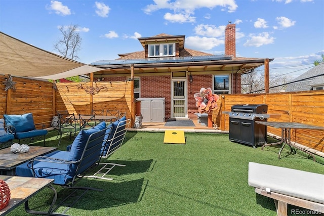 rear view of house featuring a fenced backyard, a chimney, solar panels, and brick siding