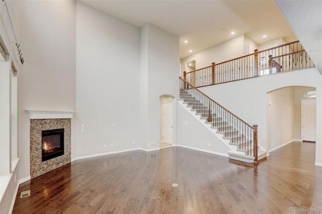 2454 Ambience Ln, Castle Rock, CO 80109 - unfurnished living room with arched walkways, a high ceiling, stairs, wood finished floors, and a tiled fireplace