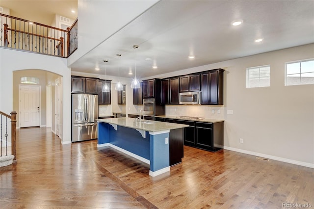 2454 Ambience Ln, Castle Rock, CO 80109 - kitchen with stainless steel appliances, a kitchen breakfast bar, light wood-style flooring, a sink, and arched walkways