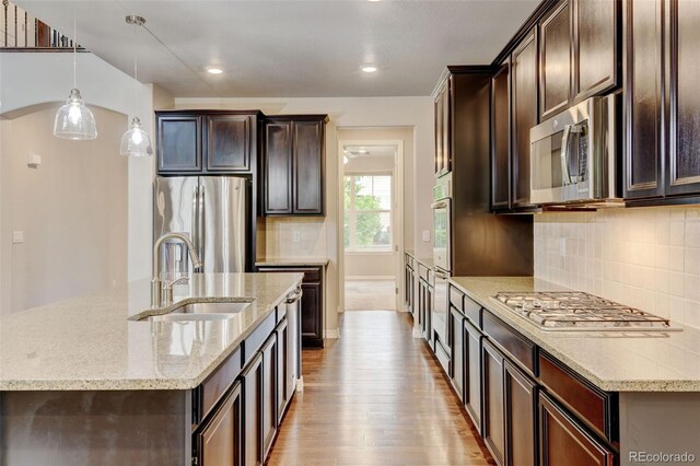 2454 Ambience Ln, Castle Rock, CO 80109 - kitchen featuring appliances with stainless steel finishes, a sink, light wood finished floors, dark brown cabinetry, and light stone counters