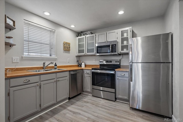 kitchen with glass insert cabinets, a sink, light wood-type flooring, gray cabinetry, and appliances with stainless steel finishes
