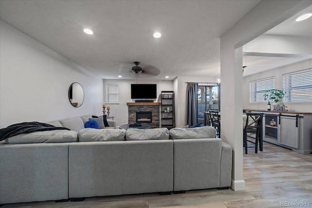 living area featuring a textured ceiling, recessed lighting, a fireplace, light wood finished floors, and a ceiling fan