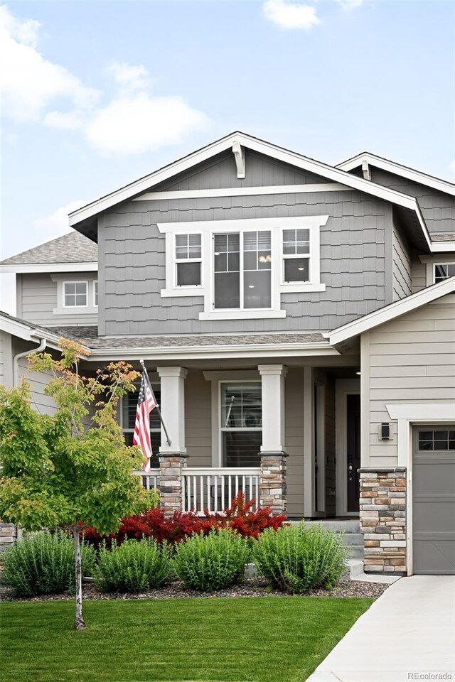 14454 Grape Way, Thornton, CO 80602 - craftsman-style house with covered porch, a front yard, a shingled roof, and stone siding