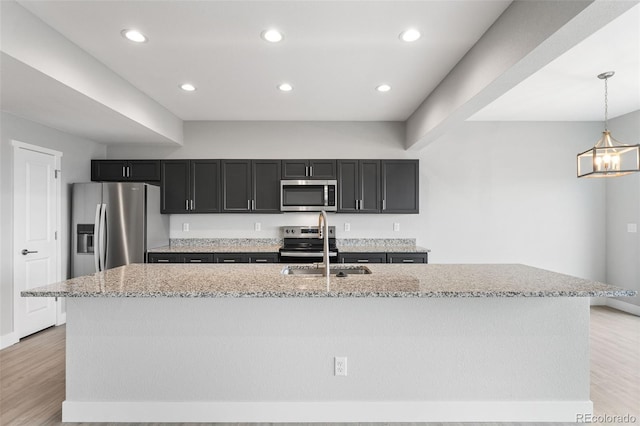 kitchen featuring an island with sink, decorative light fixtures, light hardwood / wood-style floors, light stone counters, and stainless steel appliances