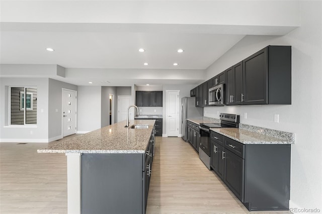 kitchen featuring light stone countertops, an island with sink, stainless steel appliances, and sink