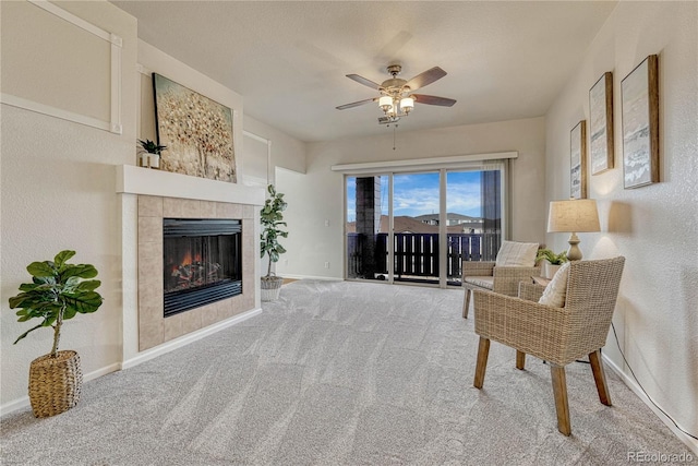 living area featuring a tiled fireplace, carpet flooring, and ceiling fan