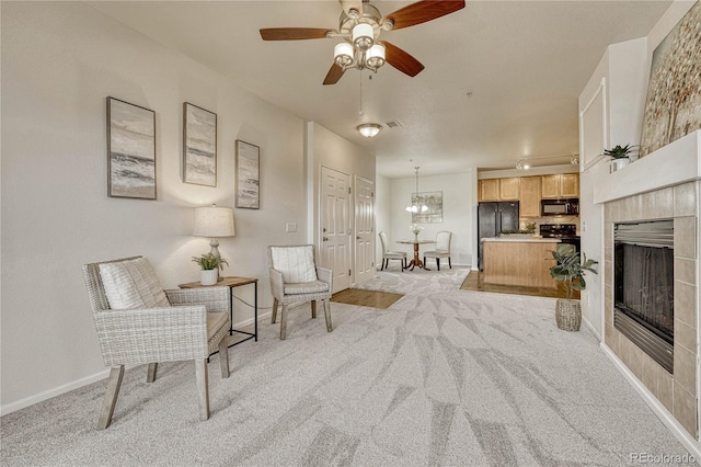 living area featuring ceiling fan, a tiled fireplace, and light carpet