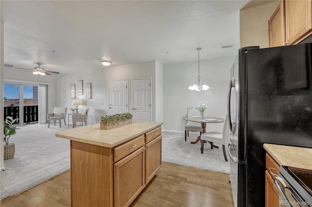 kitchen featuring ceiling fan with notable chandelier, decorative light fixtures, a center island, black fridge, and light hardwood / wood-style flooring