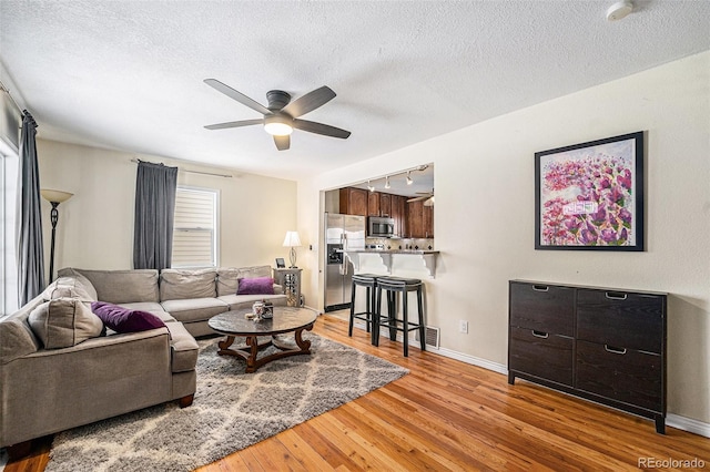 living room featuring ceiling fan, rail lighting, a textured ceiling, and light hardwood / wood-style floors