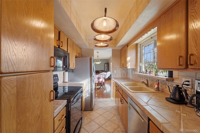 kitchen with black appliances, tile counters, sink, and a tray ceiling