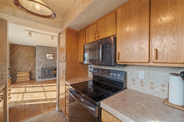 kitchen with tile countertops, wooden walls, black electric range oven, and light tile patterned floors