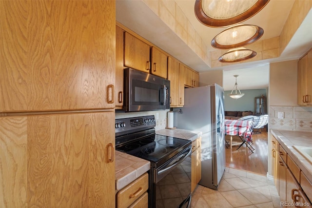 kitchen with backsplash, black / electric stove, tile counters, and light tile patterned flooring