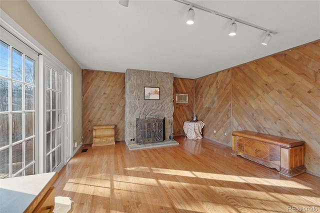 unfurnished living room featuring a fireplace, rail lighting, light hardwood / wood-style flooring, and wooden walls