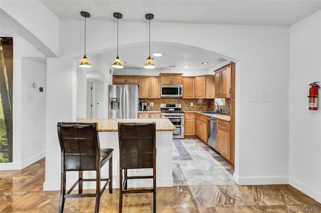 kitchen featuring backsplash, light stone counters, stainless steel appliances, sink, and pendant lighting