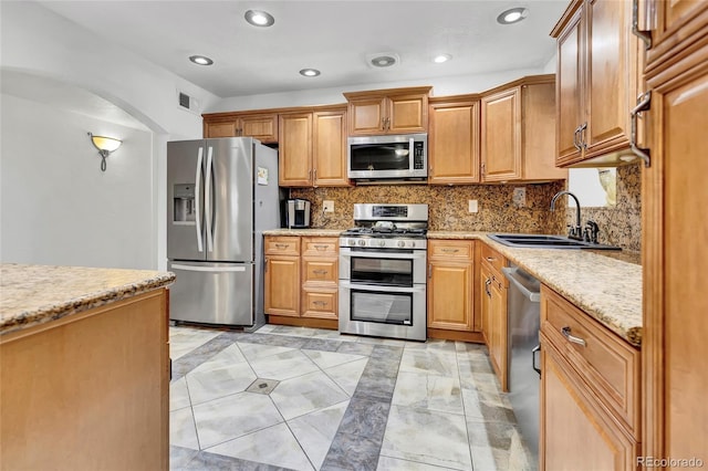 kitchen with stainless steel appliances, sink, light stone countertops, and backsplash