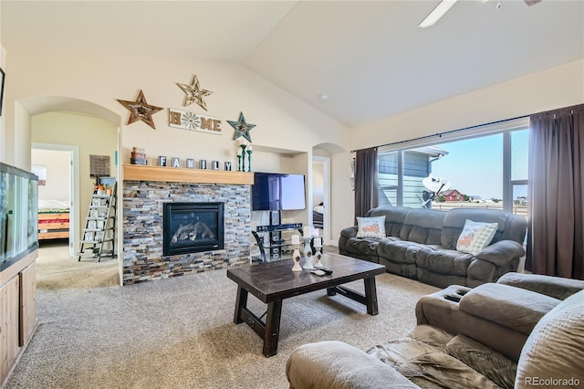 living room with high vaulted ceiling, ceiling fan, a stone fireplace, and light colored carpet