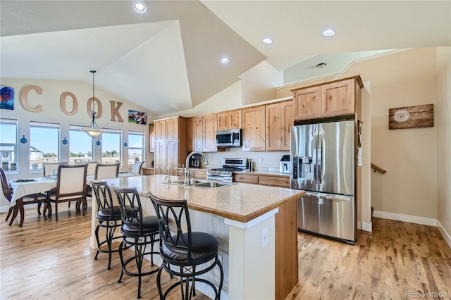 kitchen with an island with sink, lofted ceiling, sink, decorative light fixtures, and stainless steel appliances