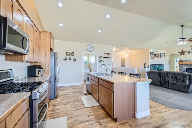 kitchen featuring an island with sink, sink, appliances with stainless steel finishes, a fireplace, and light wood-type flooring