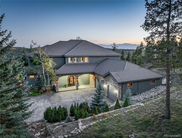 view of front of home with driveway, stone siding, an attached garage, and stucco siding