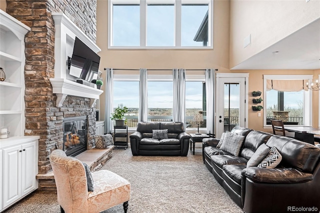 living room with a high ceiling, carpet floors, built in shelves, a stone fireplace, and a chandelier