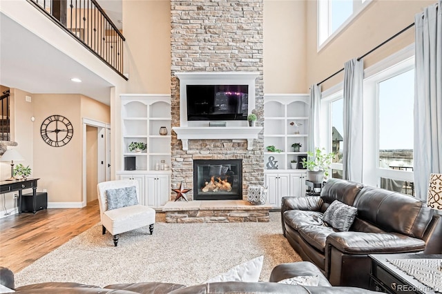 living room featuring hardwood / wood-style flooring, a towering ceiling, a stone fireplace, and built in features