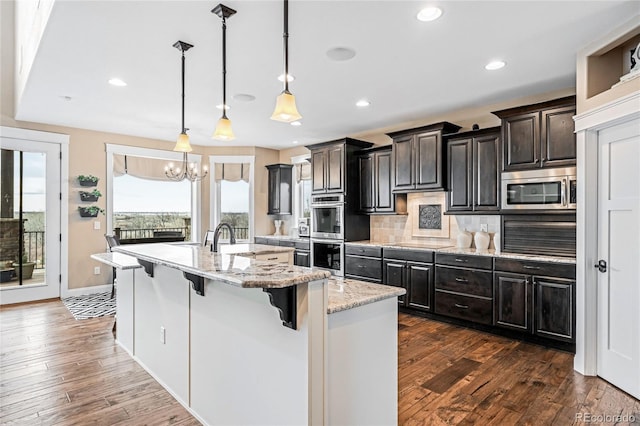 kitchen with appliances with stainless steel finishes, a breakfast bar area, hanging light fixtures, light stone countertops, and a center island with sink