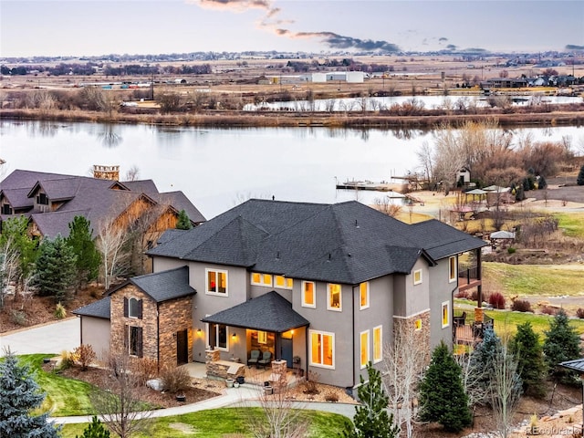 rear view of property with a water view, stucco siding, a patio area, stone siding, and driveway