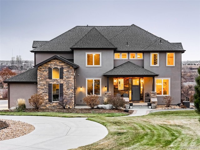 rear view of property featuring roof with shingles, a porch, stucco siding, concrete driveway, and a lawn