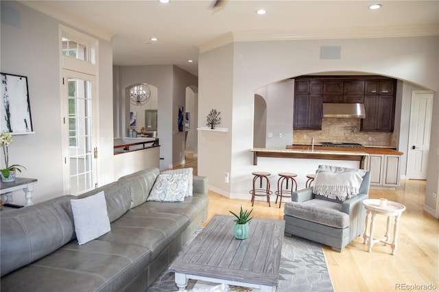 living room with light hardwood / wood-style floors, crown molding, sink, and an inviting chandelier