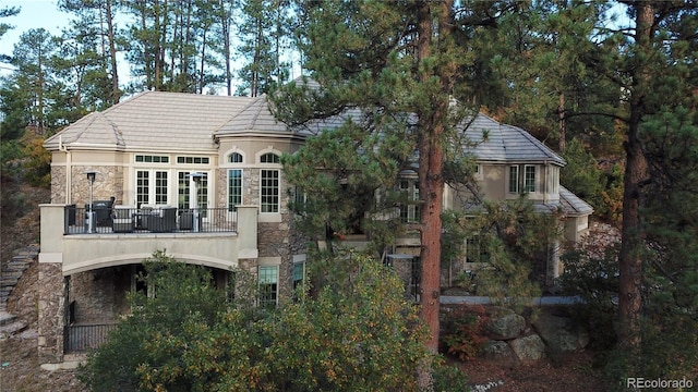 back of property featuring stone siding, a balcony, and stucco siding
