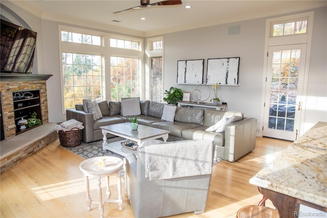 living room featuring ornamental molding, a stone fireplace, light wood-type flooring, and ceiling fan