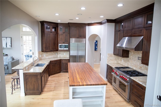 kitchen featuring ventilation hood, built in appliances, decorative backsplash, and light wood-type flooring