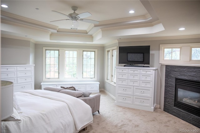 bedroom with a raised ceiling, crown molding, a glass covered fireplace, light colored carpet, and ceiling fan