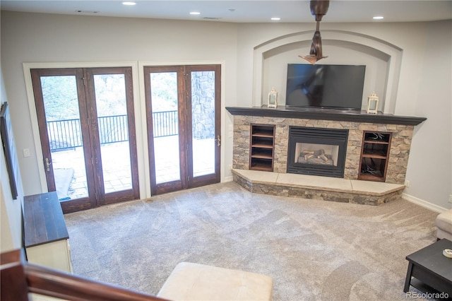 unfurnished living room featuring french doors, a stone fireplace, and carpet flooring