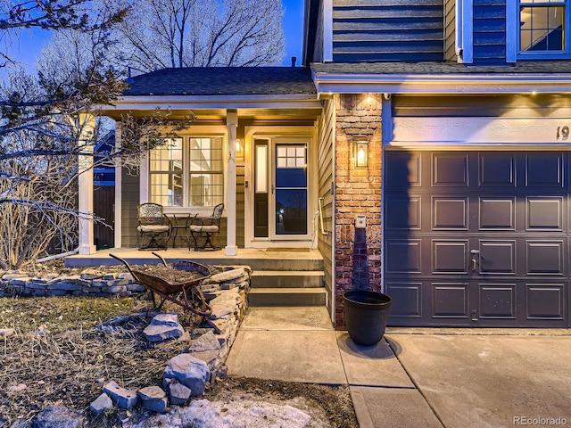 entrance to property featuring a garage, brick siding, covered porch, and a shingled roof