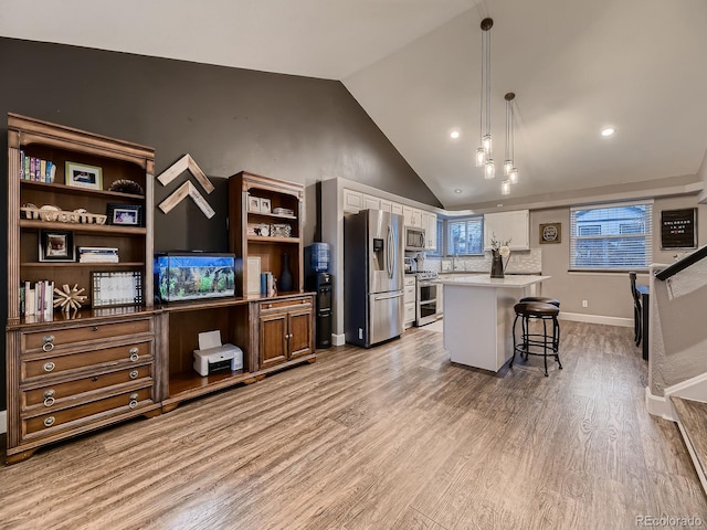 kitchen with lofted ceiling, a breakfast bar area, stainless steel appliances, light wood-style floors, and light countertops