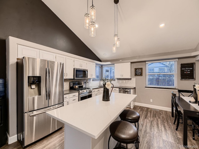 kitchen with tasteful backsplash, white cabinets, dark wood finished floors, appliances with stainless steel finishes, and a breakfast bar