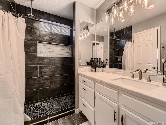 full bathroom with tiled shower, vanity, a textured ceiling, and wood finished floors