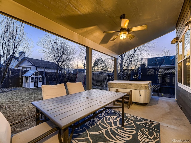 patio terrace at dusk featuring outdoor dining space, a fenced backyard, a ceiling fan, and a hot tub